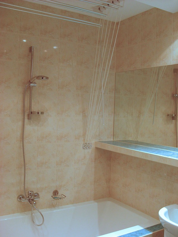 Jasna łazienka z beżowymi płytkami: wanna, prysznic, lustro i suszarka sufitowa z linkami. Widok na fragment wnętrza po remoncie.