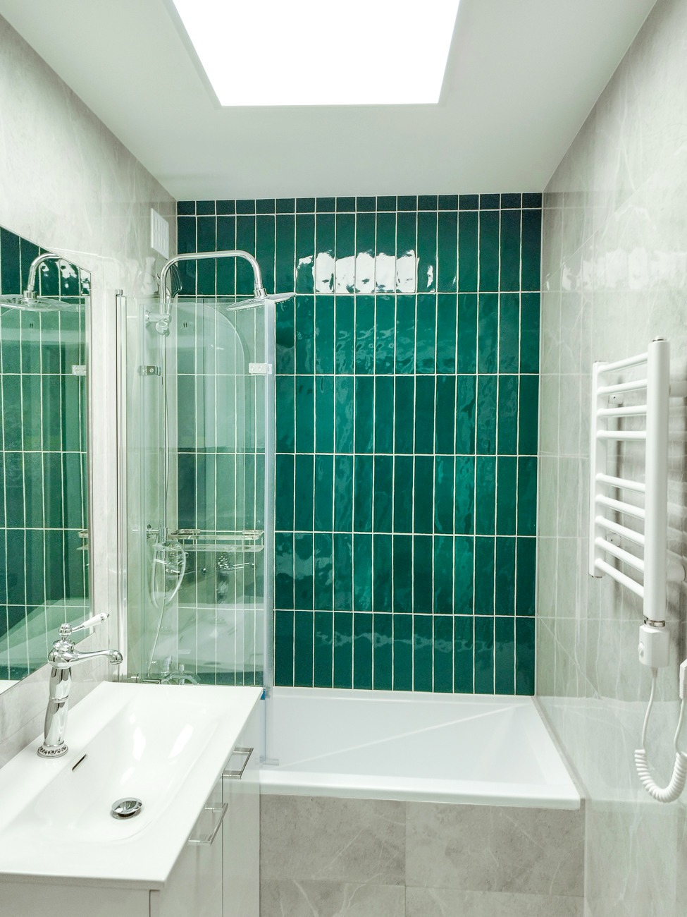 Nowoczesna łazienka z zielonymi, błyszczącymi płytkami ułożonymi pionowo, białą umywalką z chromowaną baterią i grzejnikiem drabinkowym. Całość doświetlona światłem z góry.