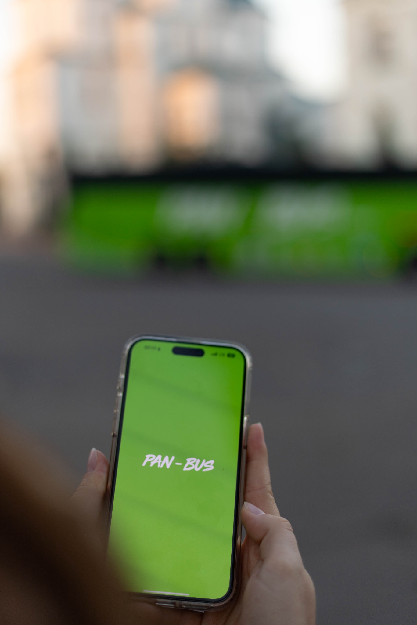Osoba trzyma telefon z logo Pan-Bus w Siechnicach. W tle rozmyty autobus, sugerujący usługi transportowe.