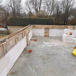 Rafał Rosiński - Wznoszenie ścian z bloczków betonu komórkowego z szalunkiem zbrojeniowym. Widoczne bloczki, szalunek, zbrojenie oraz fragment fundamentu. Prace budowlane w toku.