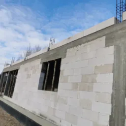 Ściany z betonu komórkowego w trakcie budowy domu jednorodzinnego w Mirowie Starym. Widoczne otwory okienne z drewnianymi stemplami i zbrojenie na górze ściany.