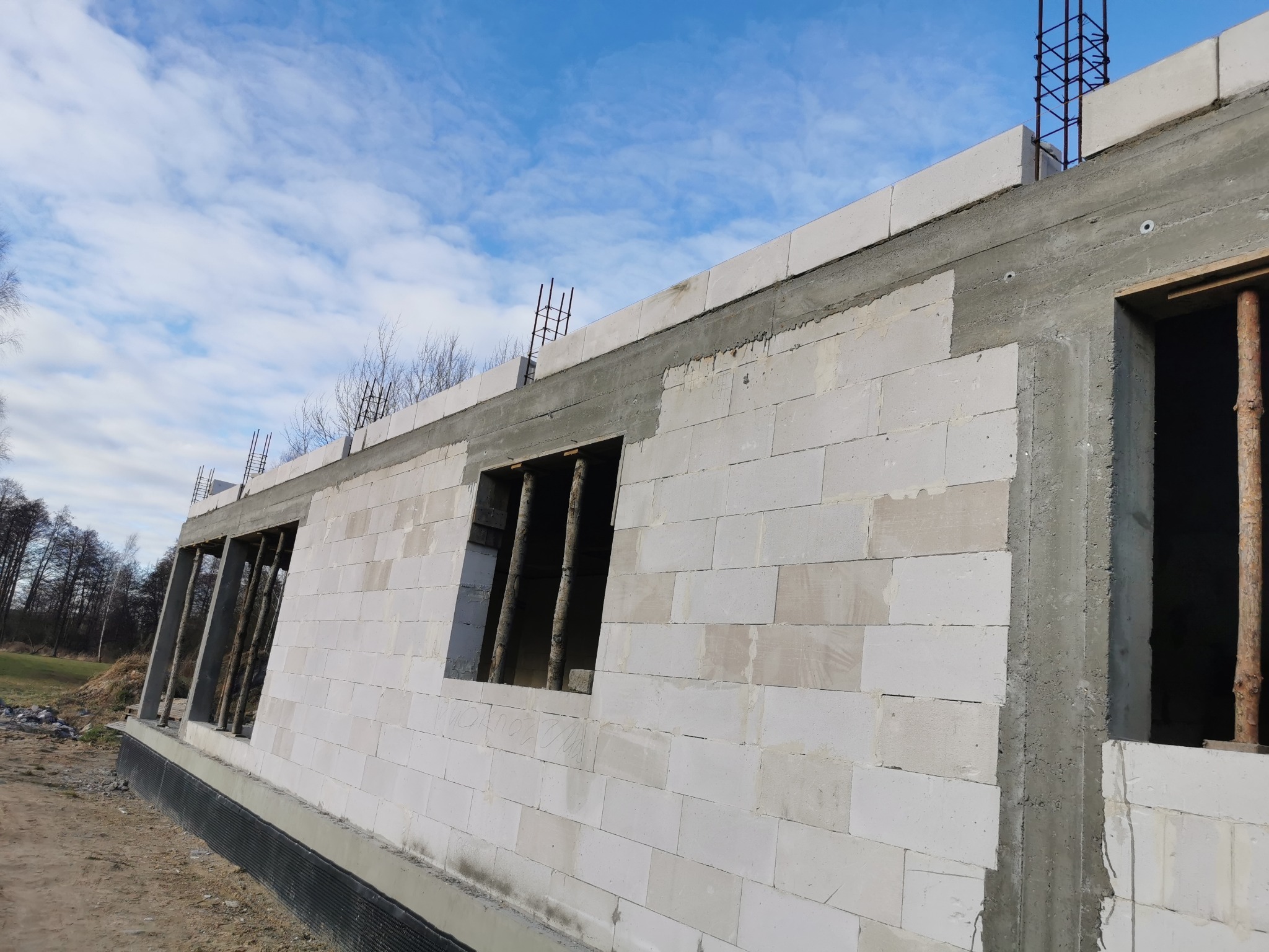 Ściany z betonu komórkowego w trakcie budowy domu jednorodzinnego w Mirowie Starym. Widoczne otwory okienne z drewnianymi stemplami i zbrojenie na górze ściany.