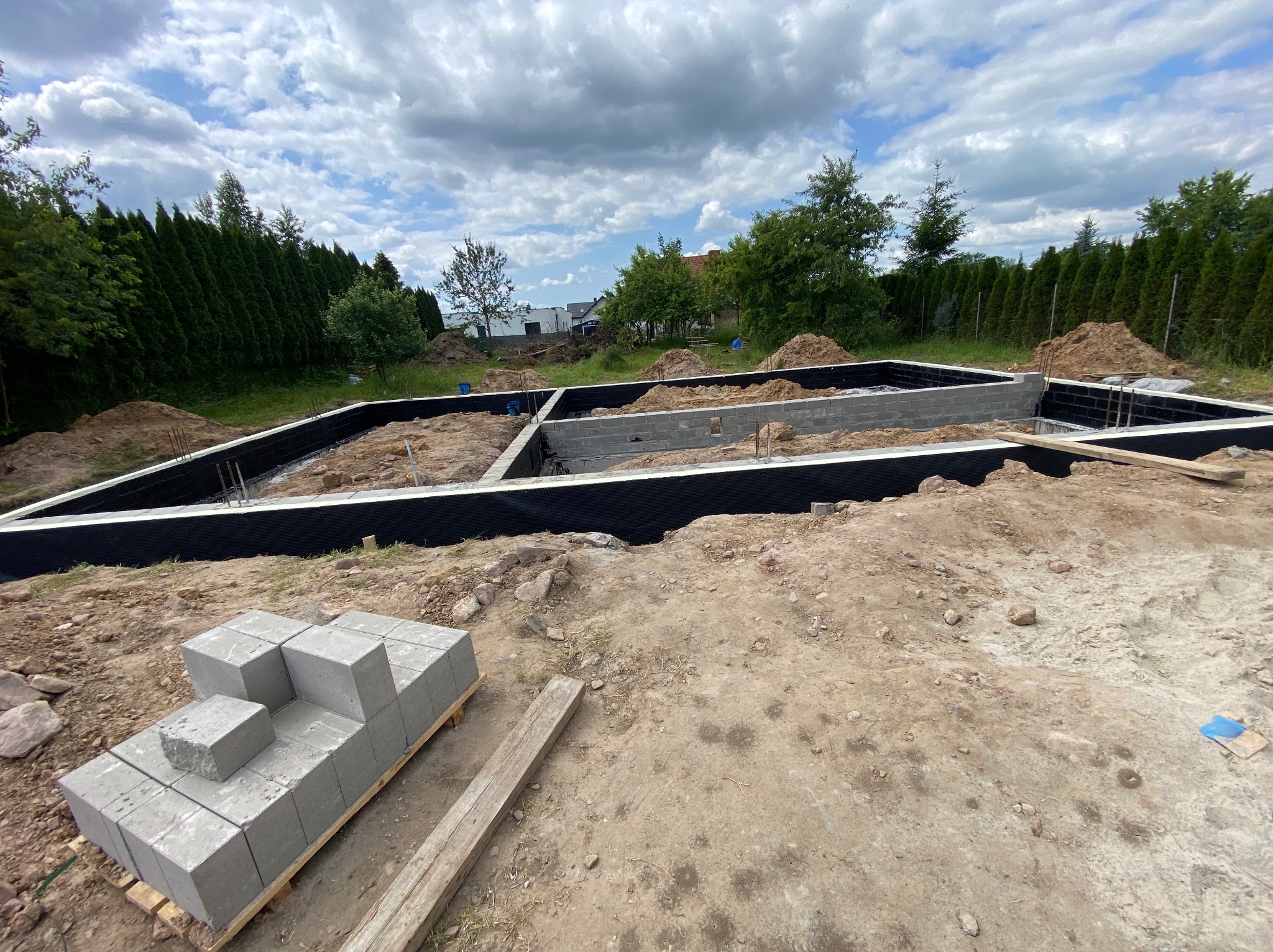 Fundamenty domu w trakcie budowy: bloczki betonowe, izolacja przeciwwilgociowa, zbrojenie. Widok z góry na plac budowy w słoneczny dzień.
