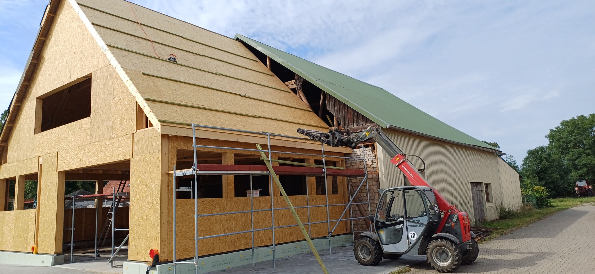 Konstrukcja dachu z desek w Szczecinie, widoczna z rusztowaniem i podnośnikiem. Część dachu pokryta zielonym materiałem. Budynek w trakcie budowy.
