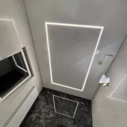 Nowoczesna łazienka z czarną marmurową podłogą i sufitem napinanym z oświetleniem LED imitującym gwiazdy, widziana z dołu, z lampą w kształcie motyla.