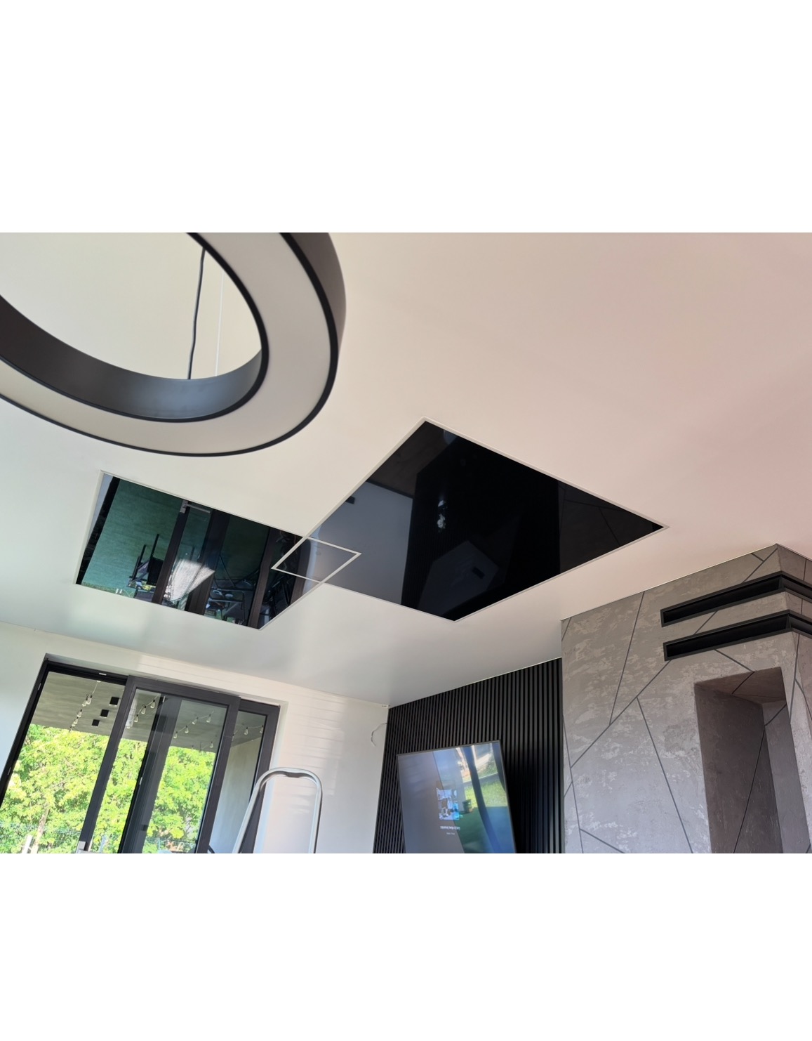 Nowoczesny sufit napinany z czarnymi, lustrzanymi wstawkami i designerską lampą w przestronnym salonie z dużym oknem i elementami dekoracyjnymi na ścianie.