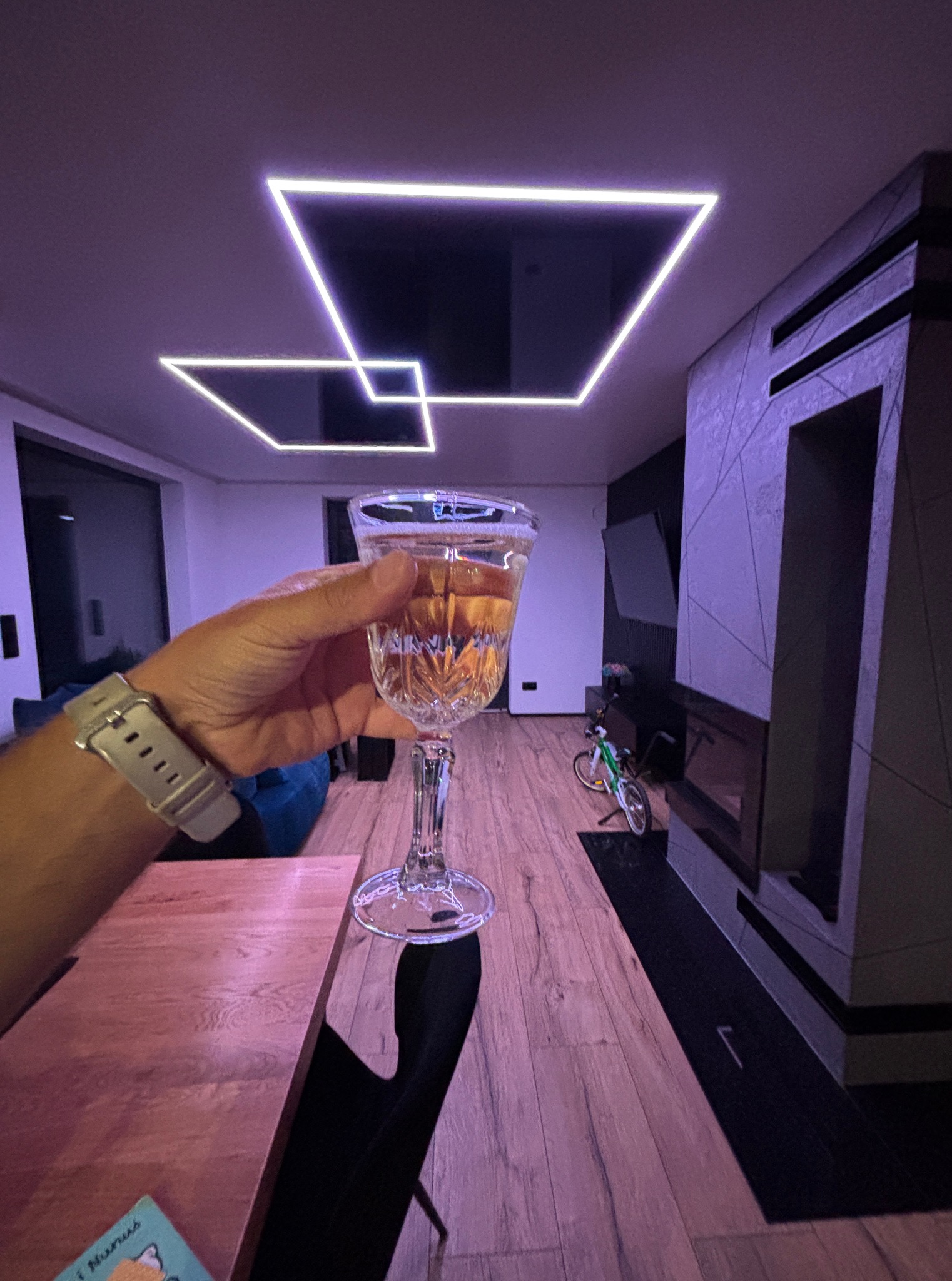 Nowoczesny salon z geometrycznymi, podświetlanymi sufitami napinanymi w kształcie kwadratów i kieliszkiem wina w dłoni, tworzącymi unikalny efekt wizualny.