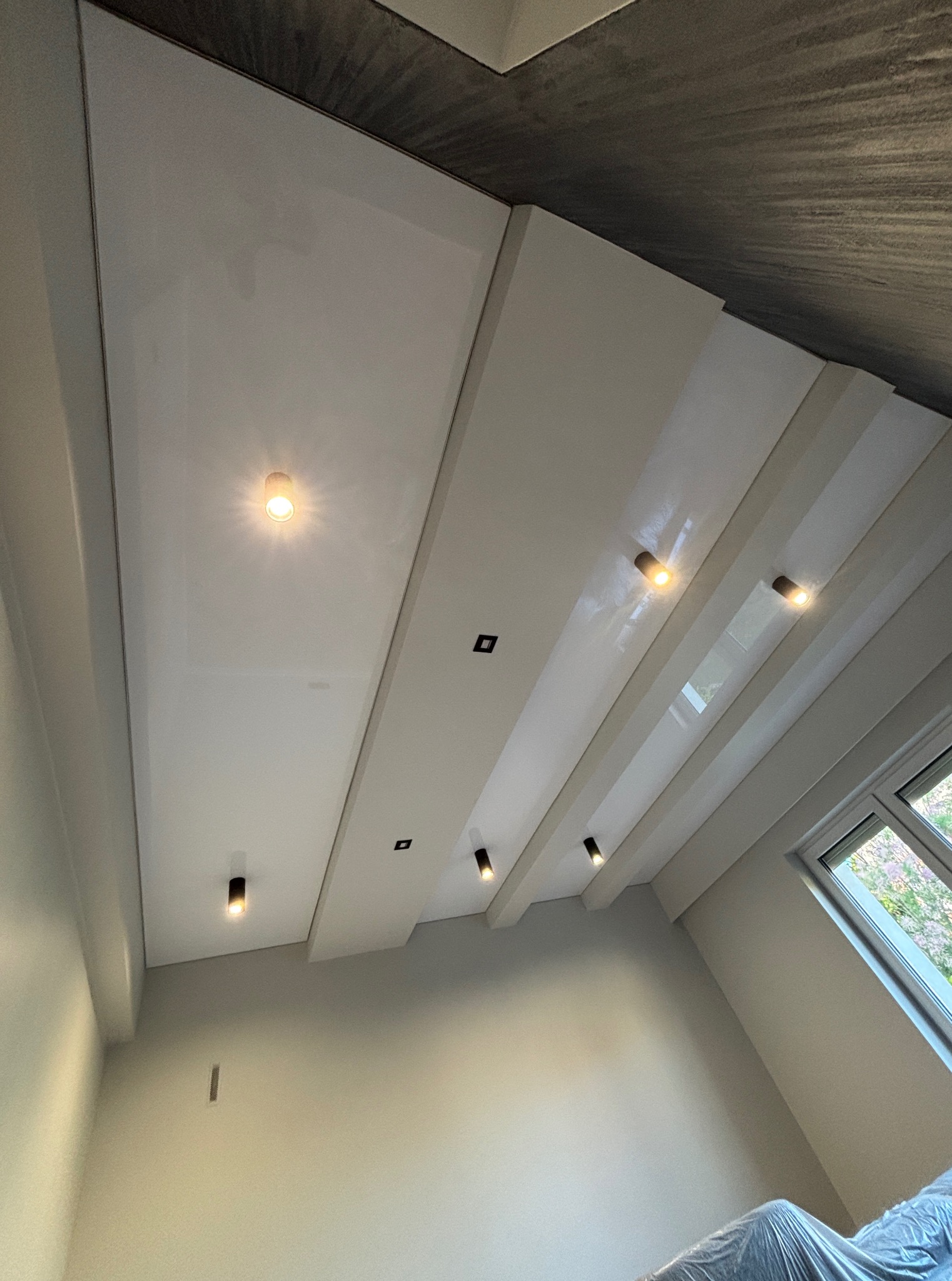 Biały sufit napinany z wbudowanym oświetleniem punktowym, widok pod kątem, fragment okna w prawym dolnym rogu. Nowoczesny design.