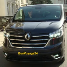Czarny bus Renault Trafic z kierowcą za szybą, zaparkowany na ulicy przed budynkiem. Widoczny numer rejestracyjny BusVoyage24.