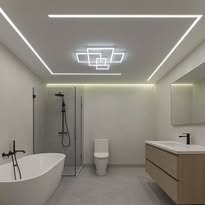 Nowoczesna łazienka z podświetlanym sufitem. Białe ściany, wanna, toaleta, umywalka z szafką. Geometryczne oświetlenie sufitowe LED.
