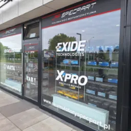 Fasada sklepu motoryzacyjnego Specpart z logo Exide i Varta na szybach, prezentująca szeroki wybór akumulatorów na półkach wewnątrz.