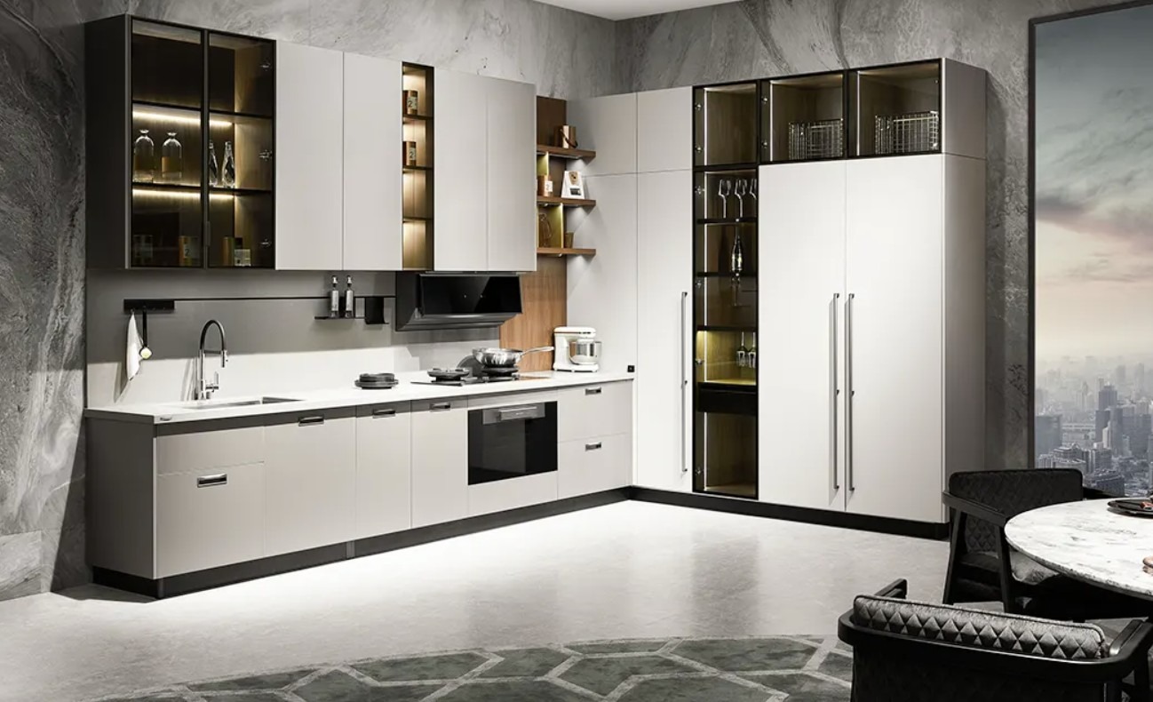 Nowoczesna kuchnia w odcieniach bieli i szarości, z przeszklonymi szafkami górnymi i subtelnym oświetleniem LED, widok na panoramę miasta przez okno.