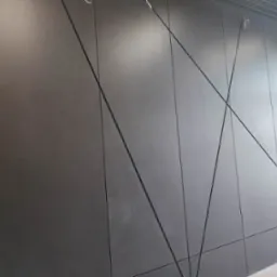 Grafitowa elewacja z paneli kompozytowych, ułożonych w geometryczny wzór. Widoczne łączenia paneli i przewody pod sufitem.