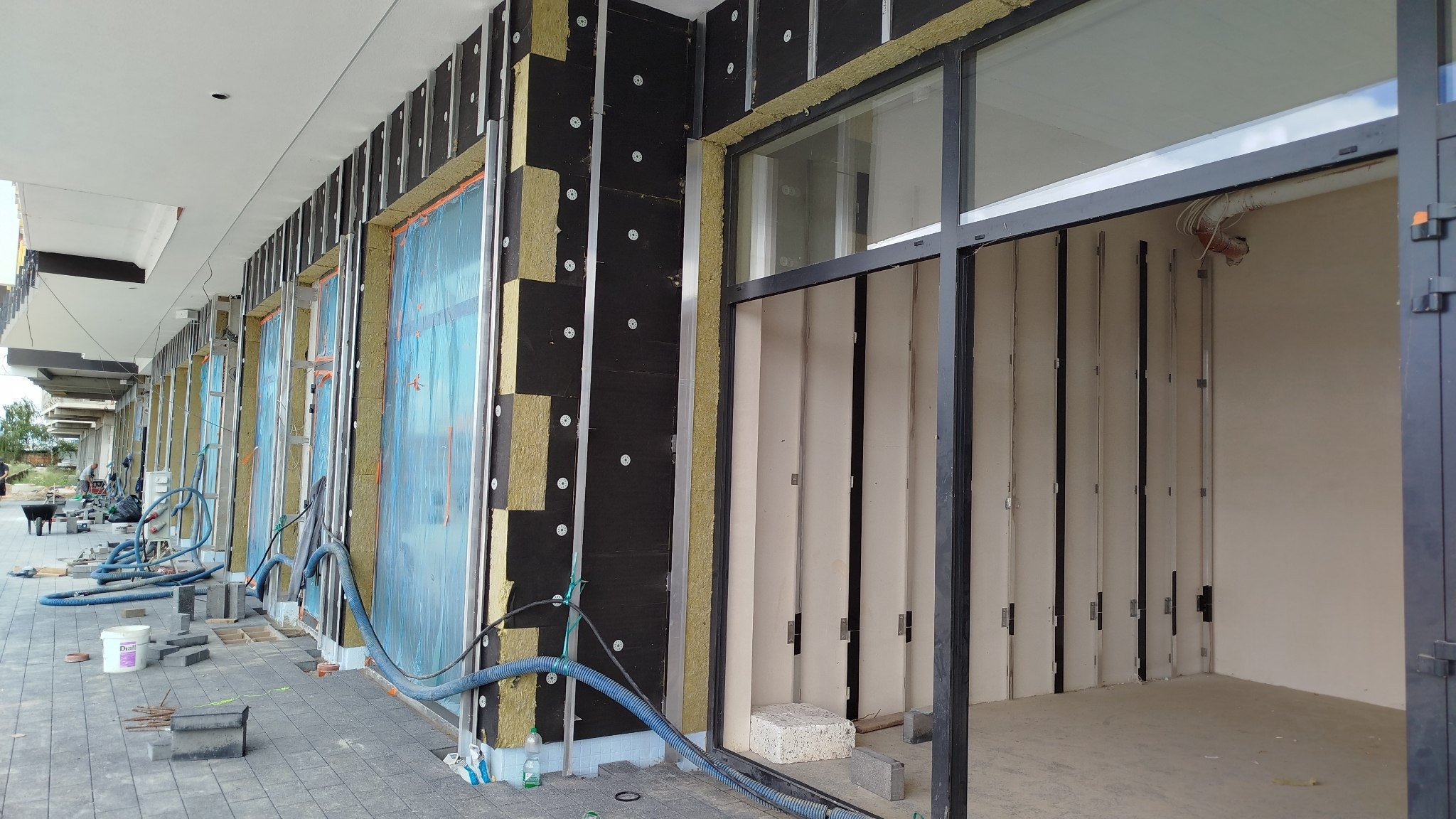 Ocieplanie budynku z widoczną warstwą izolacyjną i elementami montażowymi. Fragment elewacji z oknem w trakcie prac wykończeniowych.