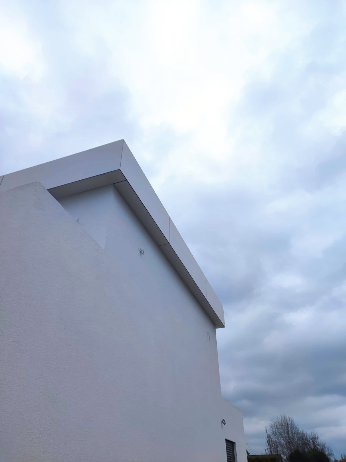 Minimalistyczna, biała elewacja budynku pod pochmurnym niebem. Detal wykończenia, kątowe ujęcie.