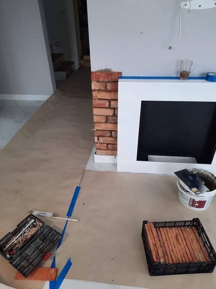 Montaż cegły dekoracyjnej przy kominku w Choczewie. Widoczne narzędzia glazurnicze, płytki i zabezpieczone podłoże.