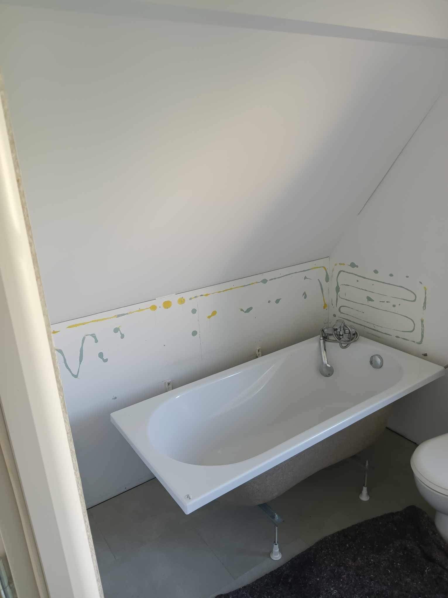 Biała wanna w łazience na poddaszu, ściany przygotowane do położenia płytek, widoczne ślady po kleju i zaznaczony kształt grzejnika.