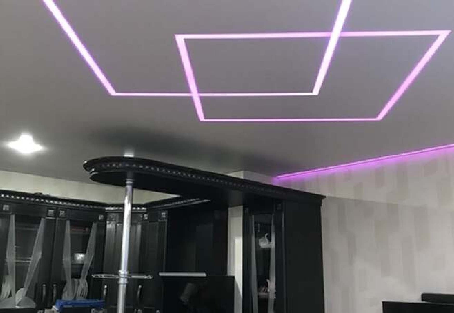 Nowoczesny, szary sufit z geometrycznym oświetleniem LED w kolorze fioletowym, widoczny fragment czarnej zabudowy meblowej.