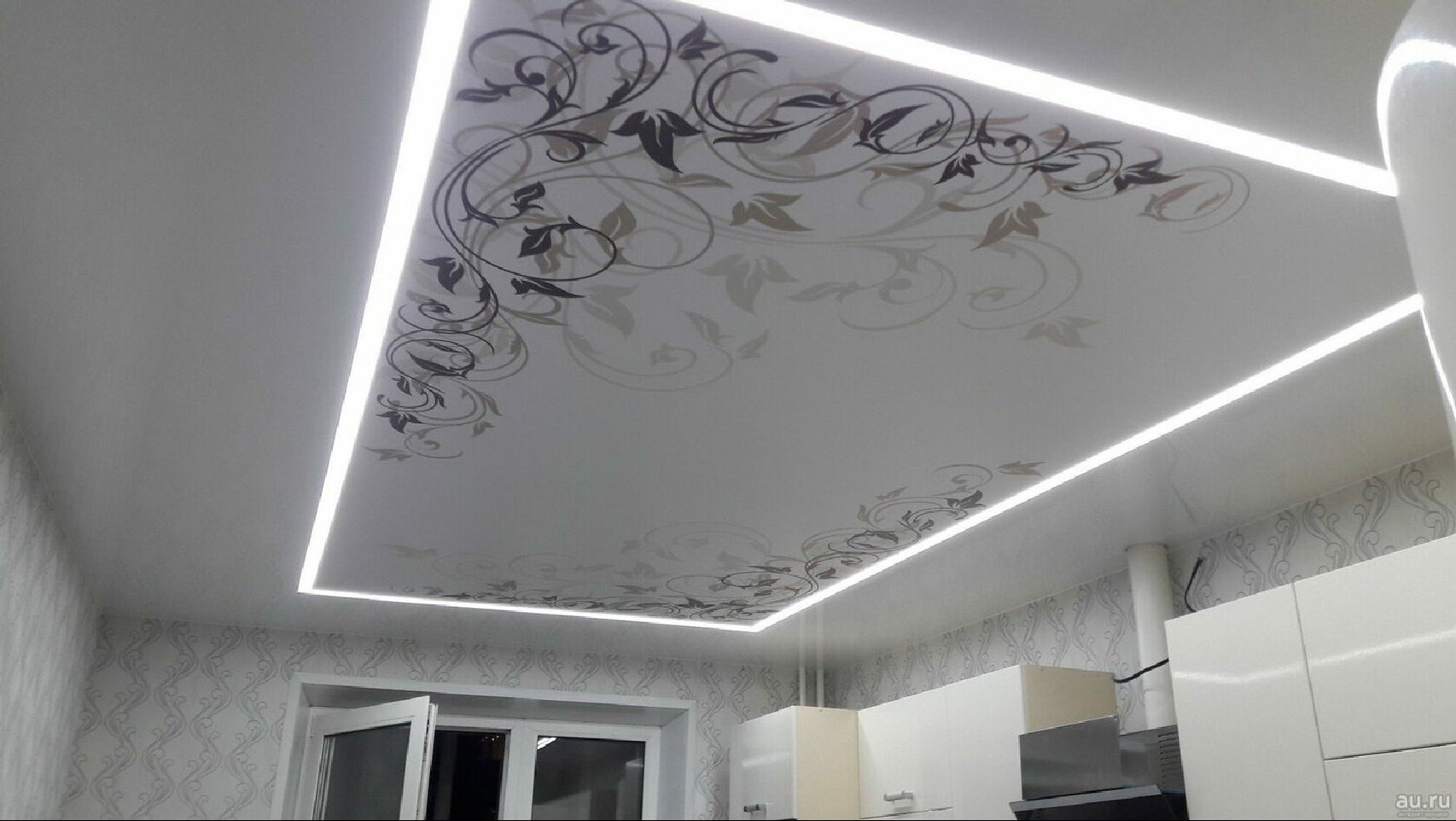 Biały sufit z motywem roślinnym, oświetleniem LED wzdłuż krawędzi, widok z dołu, fragment okna i zabudowy kuchennej w tle.