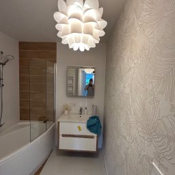 TOL-BUD Anatolii Staryk - Wykończona łazienka z wanną, umywalką i wzorzystą tapetą. Lampa w kształcie kwiatu nadaje wnętrzu nowoczesny charakter. Widoczne detale wykończenia.