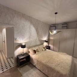 TOL-BUD Anatolii Staryk - Elegancka sypialnia po remoncie: wzorzysta tapeta, beżowe futrzane łóżko, czarne szafki nocne z lampkami i oryginalna lampa wisząca.