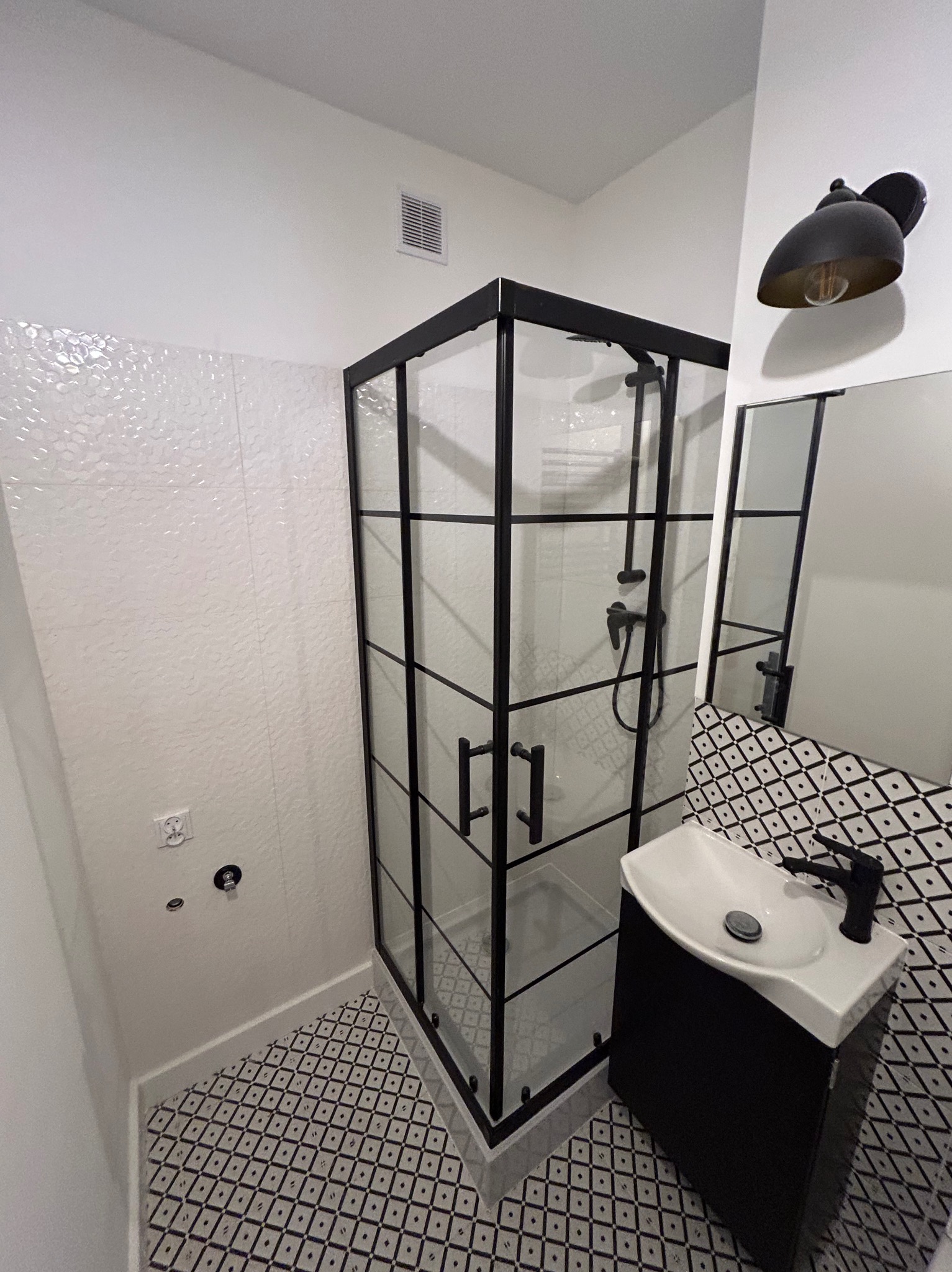 Nowoczesna łazienka w czerni i bieli: kabina prysznicowa z czarną ramą, umywalka z szafką, wzorzyste płytki podłogowe i ścienne. Minimalistyczny design.