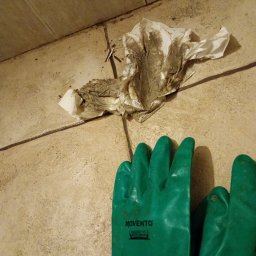 Michał - Brudna podłoga z płytek, zużyta chusteczka i zielone rękawice robocze Movento, ukazujące stan przed czyszczeniem lub remontem.