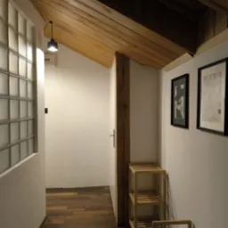 Korytarz z drewnianym sufitem i podłogą. Na ścianie szklane luksfery i grafiki w czarnych ramkach. Widoczny drewniany słupek i małe drewniane regały.
