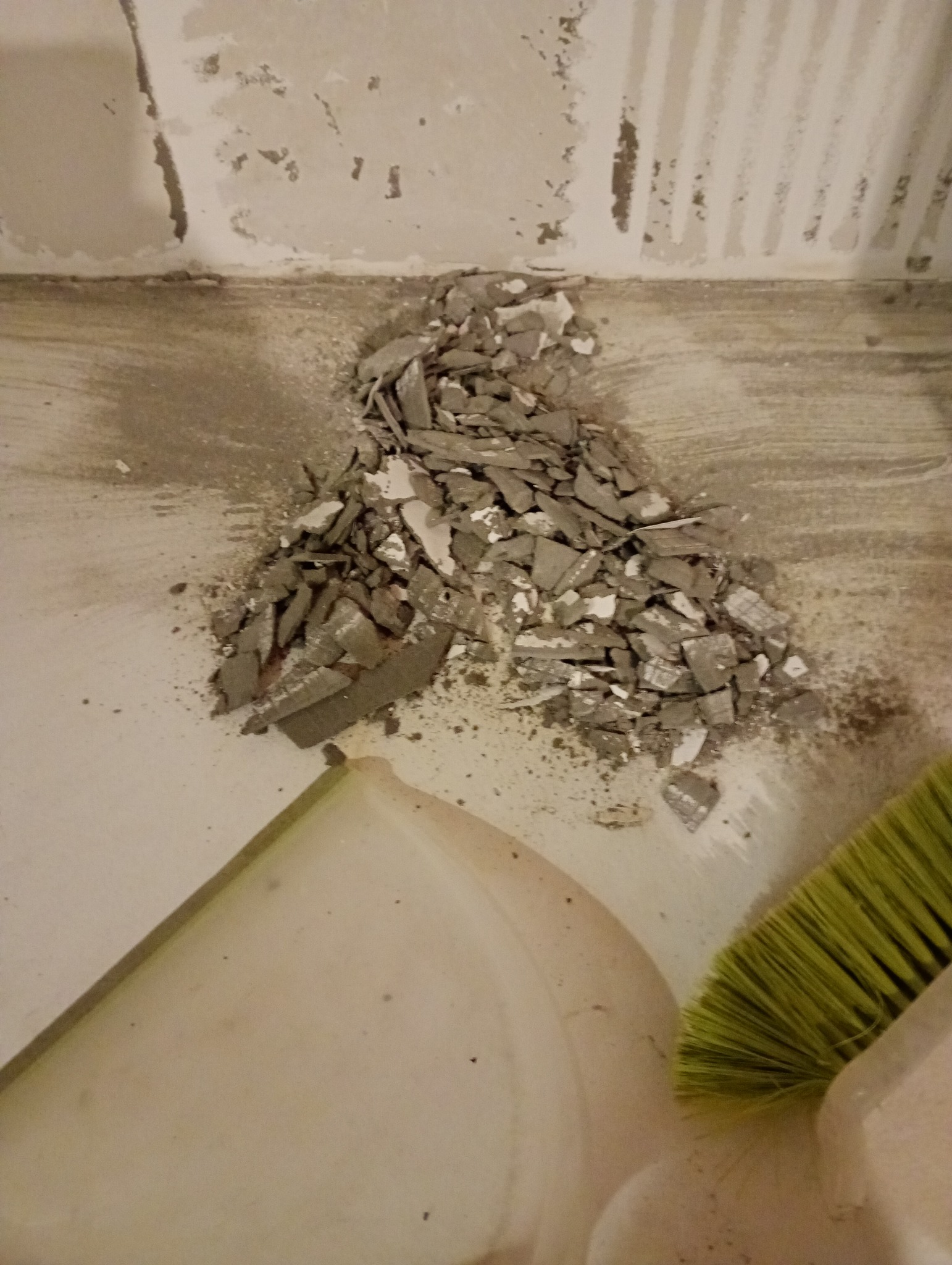 Stłuczone fragmenty płytek na podłodze, obok widoczna zmiotka i szufelka. Przygotowanie do remontu, usunięcie starej glazury w trakcie prac remontowych.