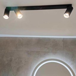 Dom na poziomie - Wykończenia wnętrz Łukasz Burzyński - Nowoczesne oświetlenie sufitowe z trzema reflektorami w łazience z szarą płytką i lustrem w Poznaniu. Minimalistyczny design, ciepłe światło.