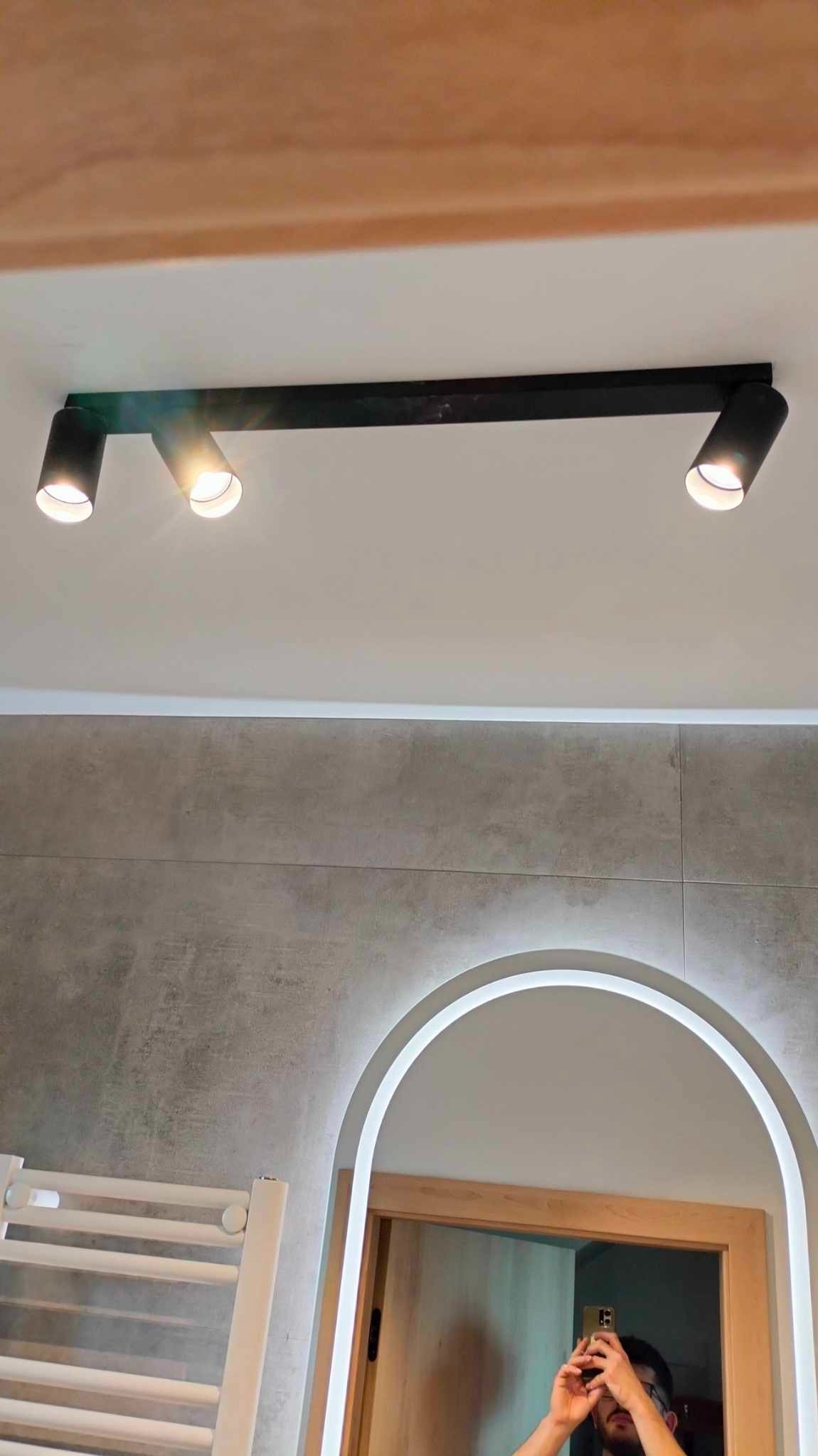 Nowoczesne oświetlenie sufitowe z trzema reflektorami w łazience z szarą płytką i lustrem w Poznaniu. Minimalistyczny design, ciepłe światło.