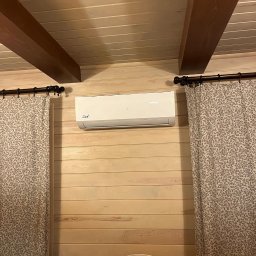 INSTAL-BUD KONRAD ZALECH - Biały klimatyzator z napisem 'Cool' zamontowany na drewnianej ścianie w pokoju. Widoczne zasłony i fragment lampki nocnej.