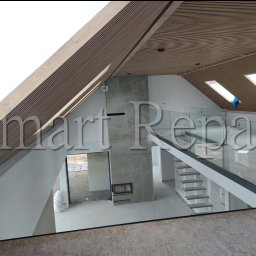 Smart Repair Oleksandr Honcharenko - Wnętrze domu w stylu nowoczesnym z drewnianym sufitem, betonowym kominkiem i szklaną balustradą schodów. Widok z góry na przestrzeń w trakcie wykańczania.