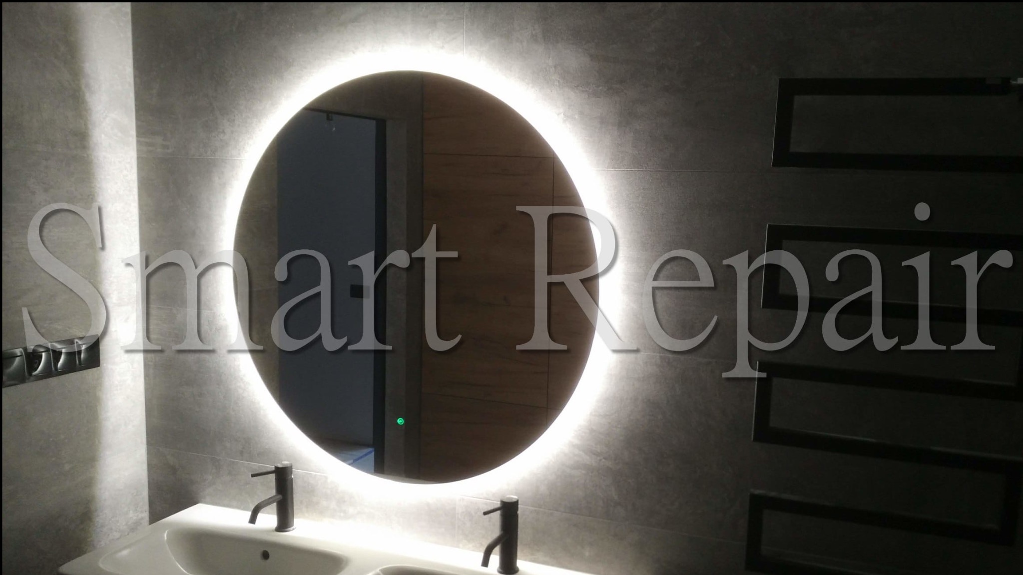 Nowoczesna łazienka z okrągłym lustrem LED, szarą płytką i białą umywalką. Widoczny grzejnik drabinkowy i minimalistyczna armatura.