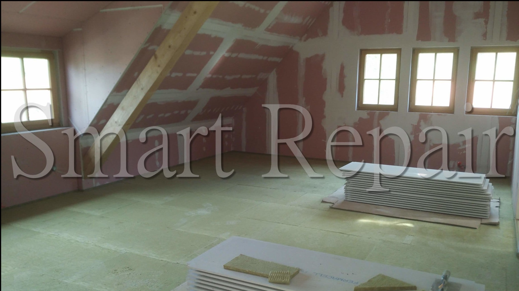 Poddasze w trakcie prac wykończeniowych: ściany po szpachlowaniu, izolacja na podłodze, płyty Fermacell czekają na montaż, trzy okna w drewnianej ramie.