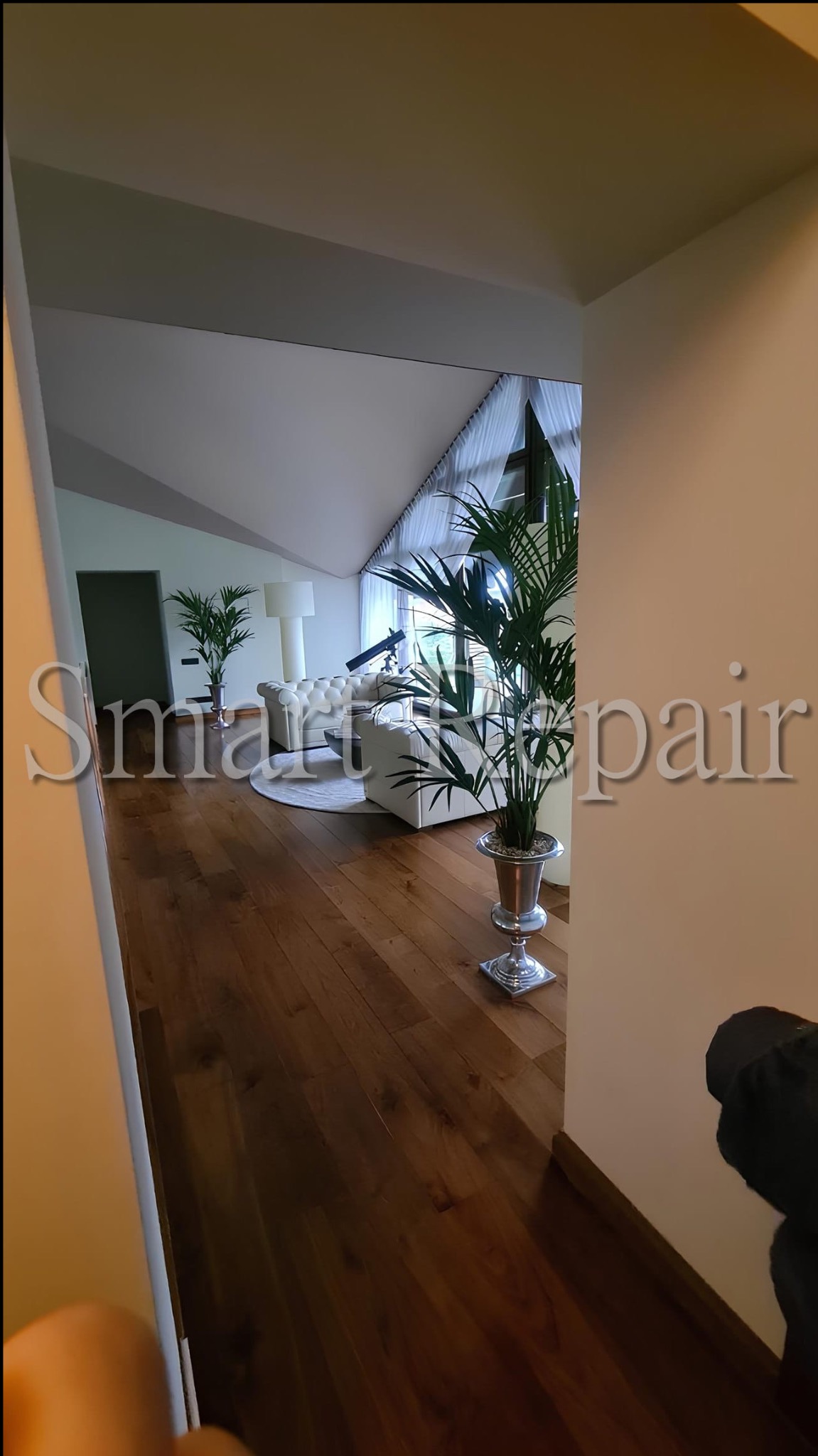 Stylowe wykończenie wnętrza poddasza z drewnianą podłogą, białymi meblami i roślinami w srebrnych donicach. Ujęcie zza rogu, widok na salon z teleskopem.