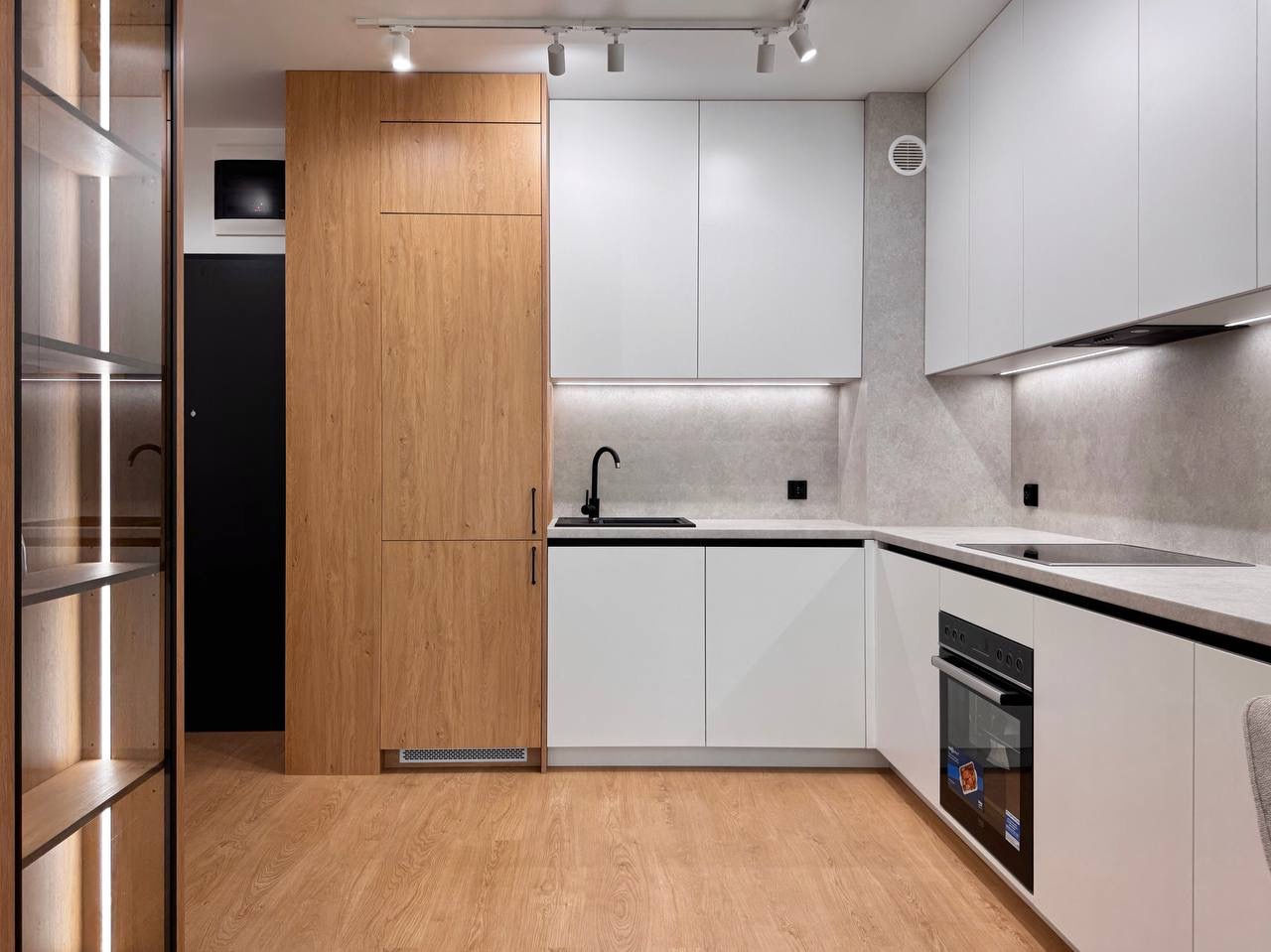 Nowoczesna kuchnia w bieli i drewnie: zabudowa meblowa z oświetleniem LED, czarna armatura, jasna podłoga. Minimalistyczny design.