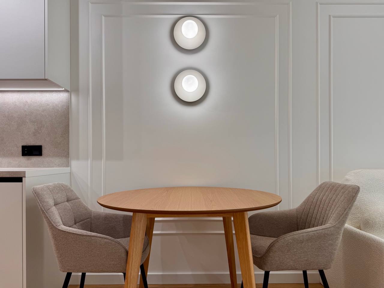 Jasne wnętrze z okrągłym stołem i krzesłami na tle ściany z dekoracyjnymi panelami i okrągłymi lampami. Minimalistyczny design.