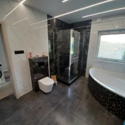 Nowoczesna łazienka z kabiną prysznicową typu walk-in, podświetleniem LED i marmurowymi płytkami. Uwagę zwraca nietypowa wanna z mozaiką.