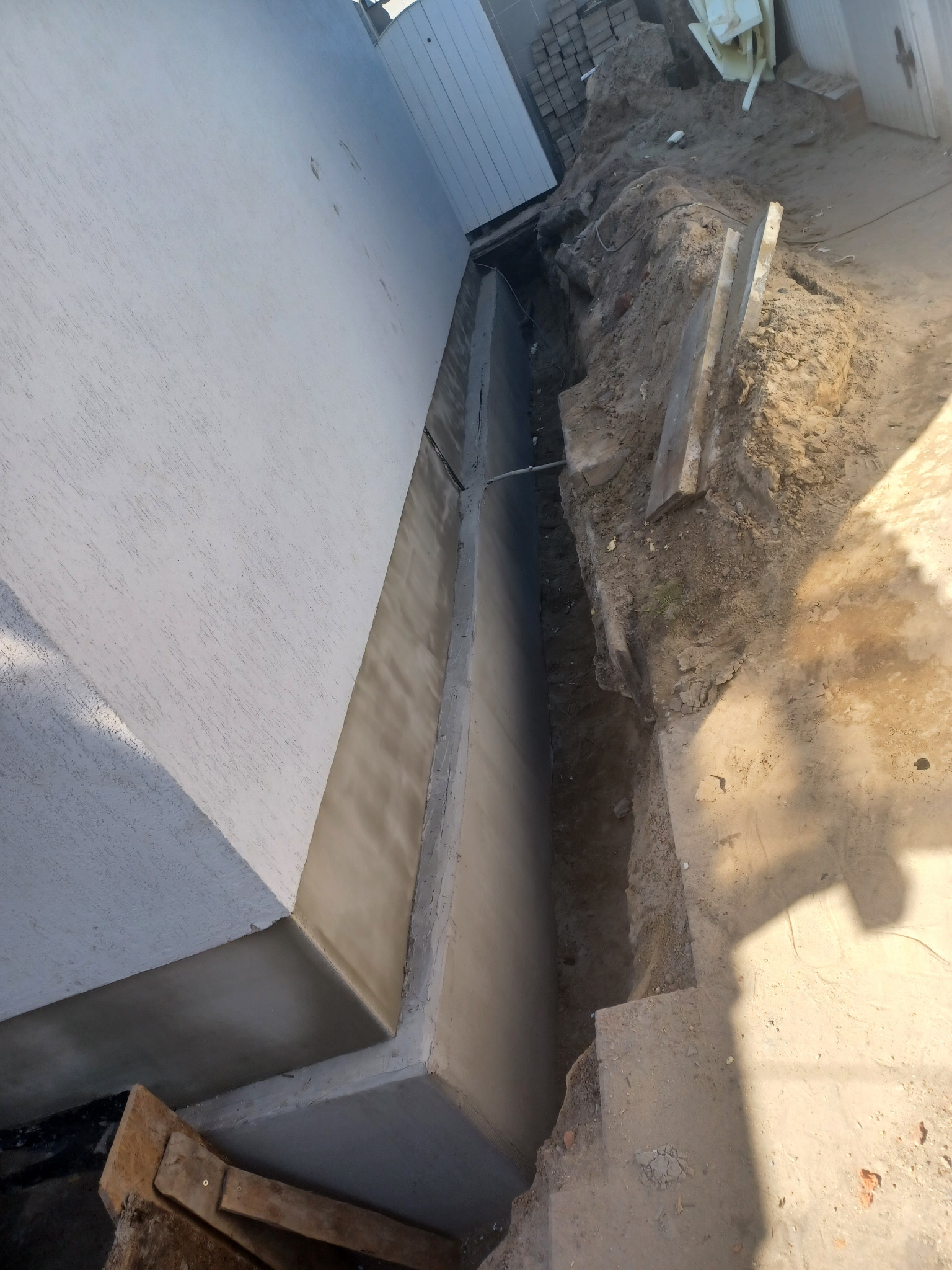 Ściana budynku z wykopem obok fundamentu. Widoczne elementy konstrukcyjne i przygotowanie do prac ziemnych. Detal z budowy.