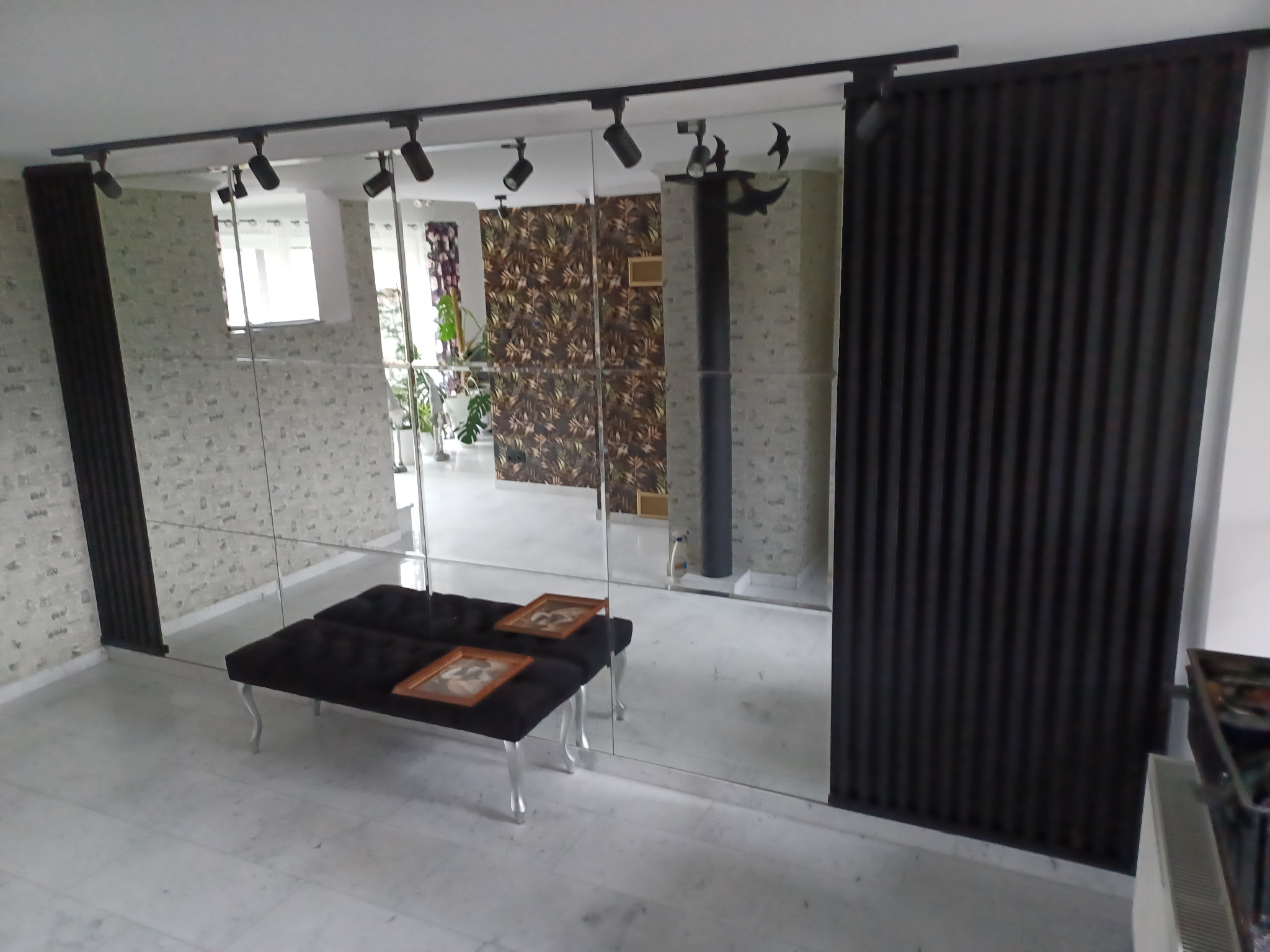 Nowoczesne wykończenie wnętrza z lustrzaną ścianą, czarnymi panelami dekoracyjnymi i oświetleniem punktowym. Na pierwszym planie czarna ławka z obrazami.