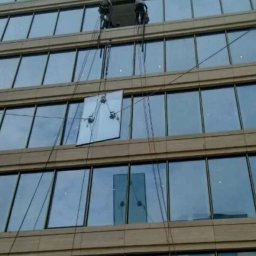 ProALPINISTA Kyrylo Rozhentsov - Dwóch pracowników na linach czyści okna wieżowca. Na środku okno z przyssawkami, liny i odbicie w oknach. Ujęcie z dołu na budynek.