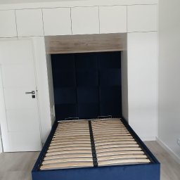 STOLMAR - Niebieskie łóżko tapicerowane ze stelażem, wbudowane w białą zabudowę meblową z szafkami. Wezgłowie z paneli tapicerowanych. Minimalistyczne wnętrze.