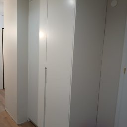 STOLMAR - Wnętrze z zabudowaną, białą szafą wnękową z subtelnymi, pionowymi uchwytami. Jasna podłoga i ściany tworzą minimalistyczny, nowoczesny wygląd.