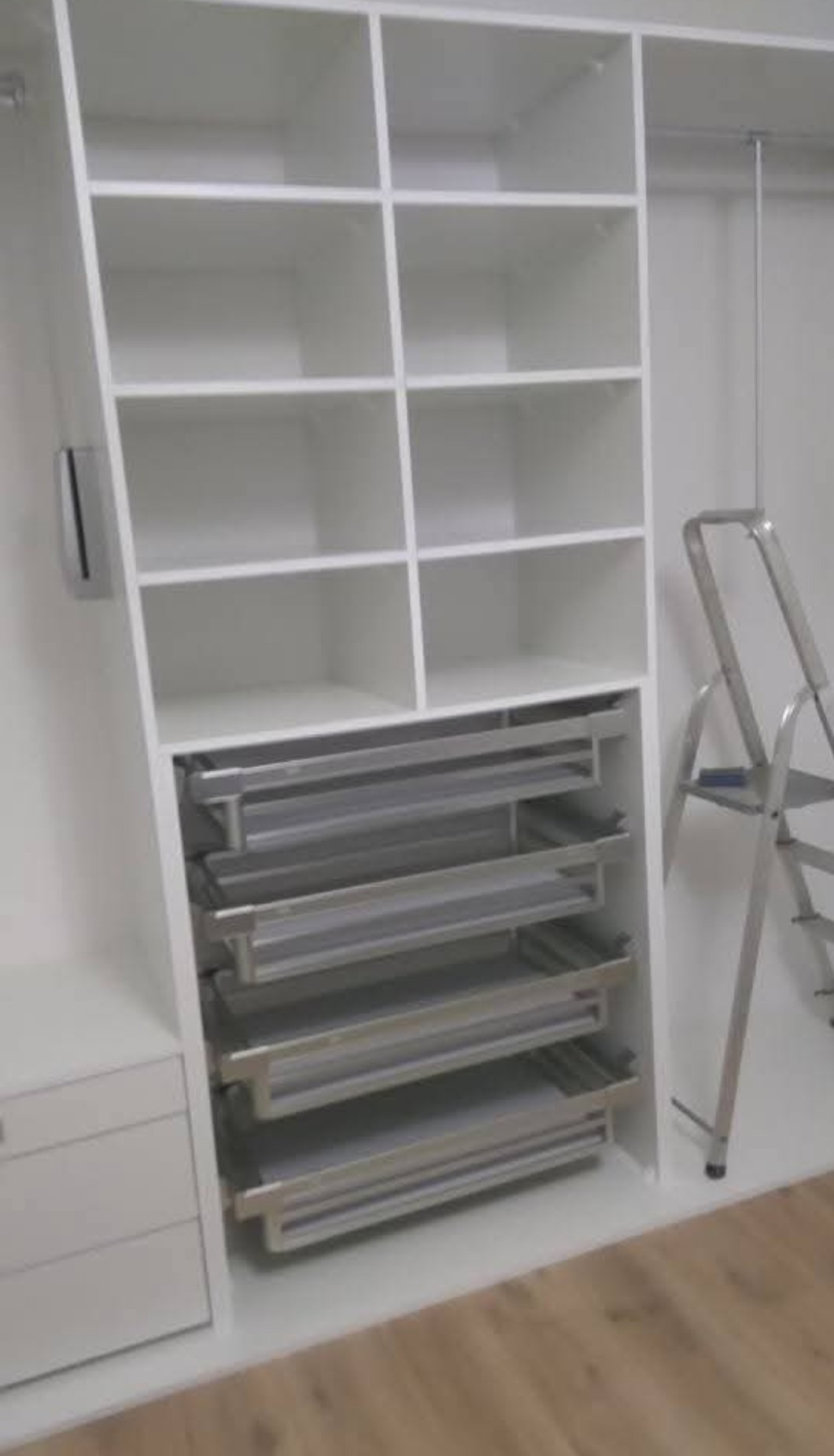 Biała szafa wnękowa z otwartymi półkami i wysuwanymi szufladami na metalowych prowadnicach. Obok drabina.