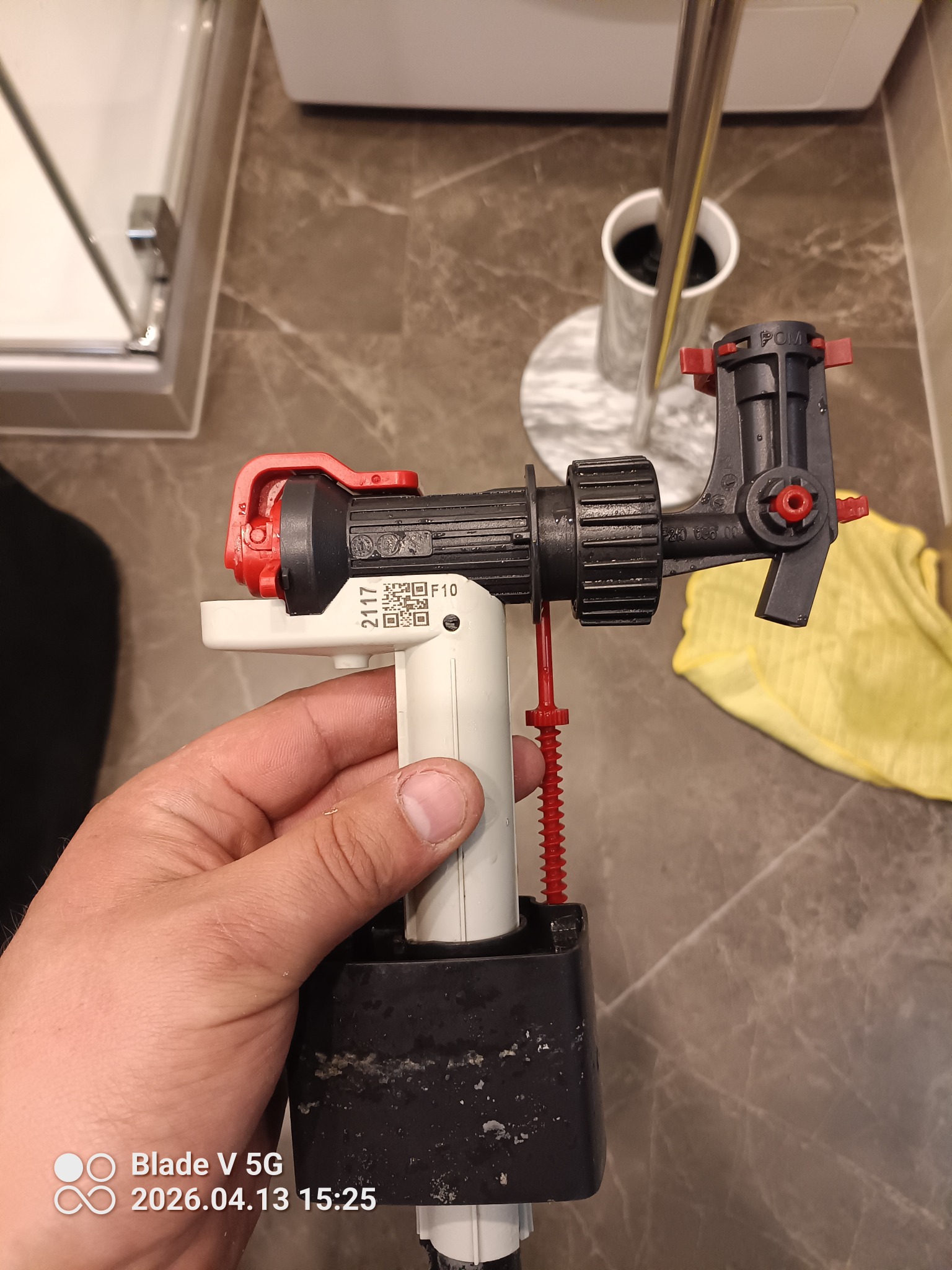 Czyszczony zawór spłuczki WC w dłoni na tle marmurowej podłogi i toalety. Widoczne osady i elementy regulacyjne. Ujęcie z bliska, podkreślające detale.