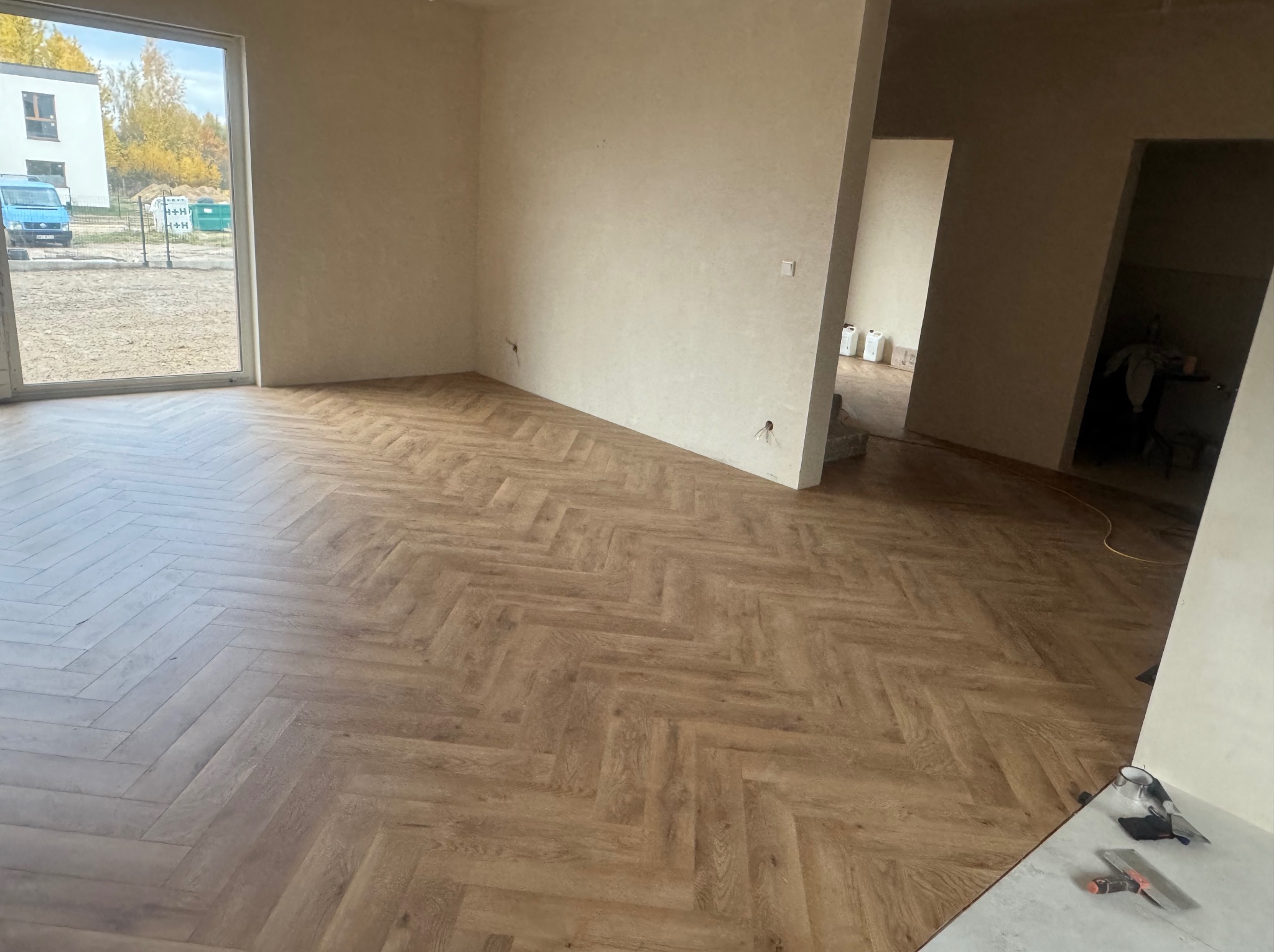 Ułożona podłoga z paneli w jodełkę w jasnym, przestronnym wnętrzu. Widoczne narzędzia i resztki materiałów, co sugeruje trwający proces wykończeniowy.