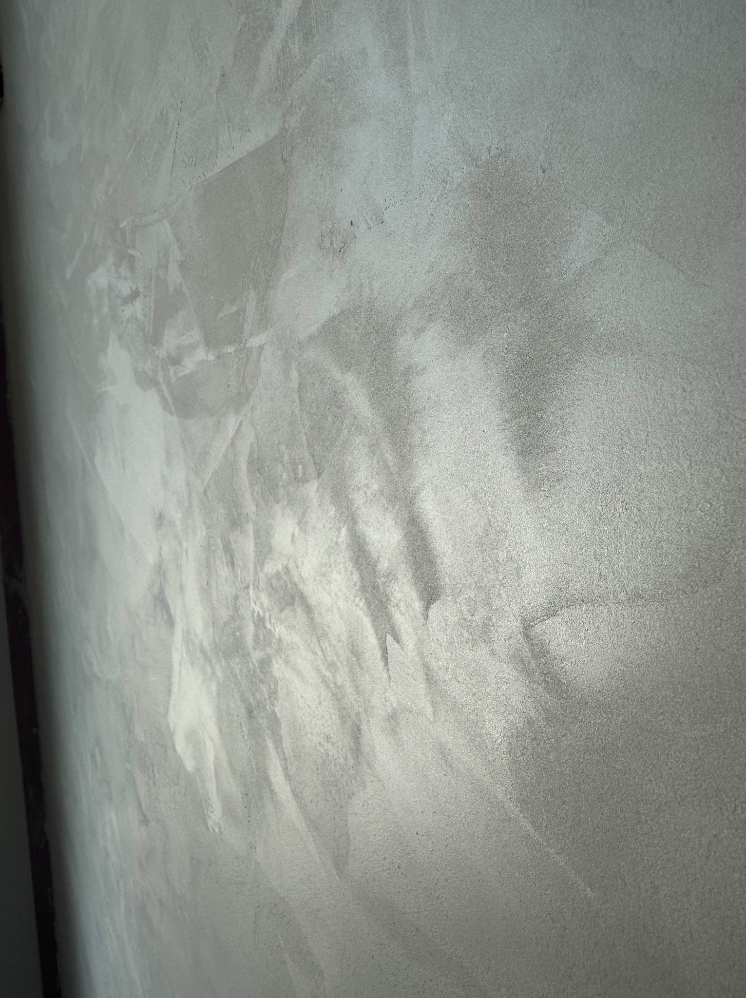 Szara ściana z efektem dekoracyjnym, imitującym beton. Widoczne nieregularne wzory i faktura. Ujęcie z boku, podkreślające strukturę powierzchni.