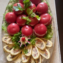 Elegancka kompozycja: pomidory faszerowane i roladki z farszem na srebrnej tacy, udekorowane sałatą i rzodkiewką. Idealne na przyjęcie.