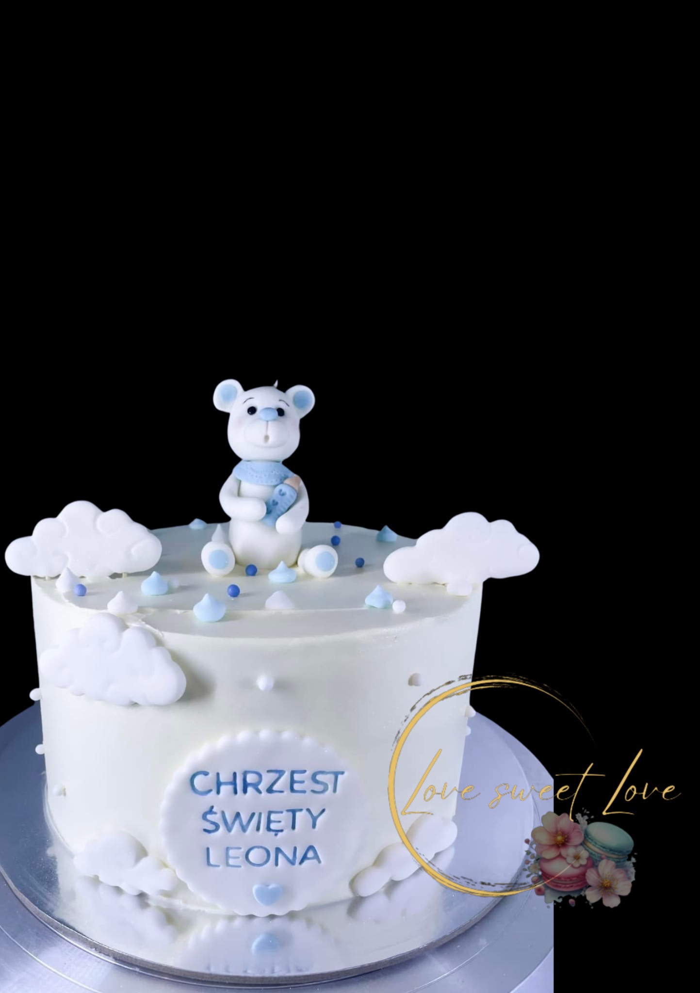 Tort na Chrzest Święty z białym lukrem, dekorowany chmurkami, niebieskimi akcentami i figurką misia. Napis 'Chrzest Święty Leona'.